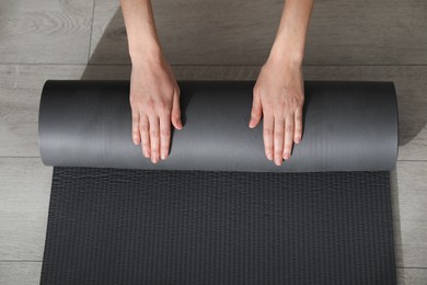Photo of Top view of woman rolling yoga mat on floor