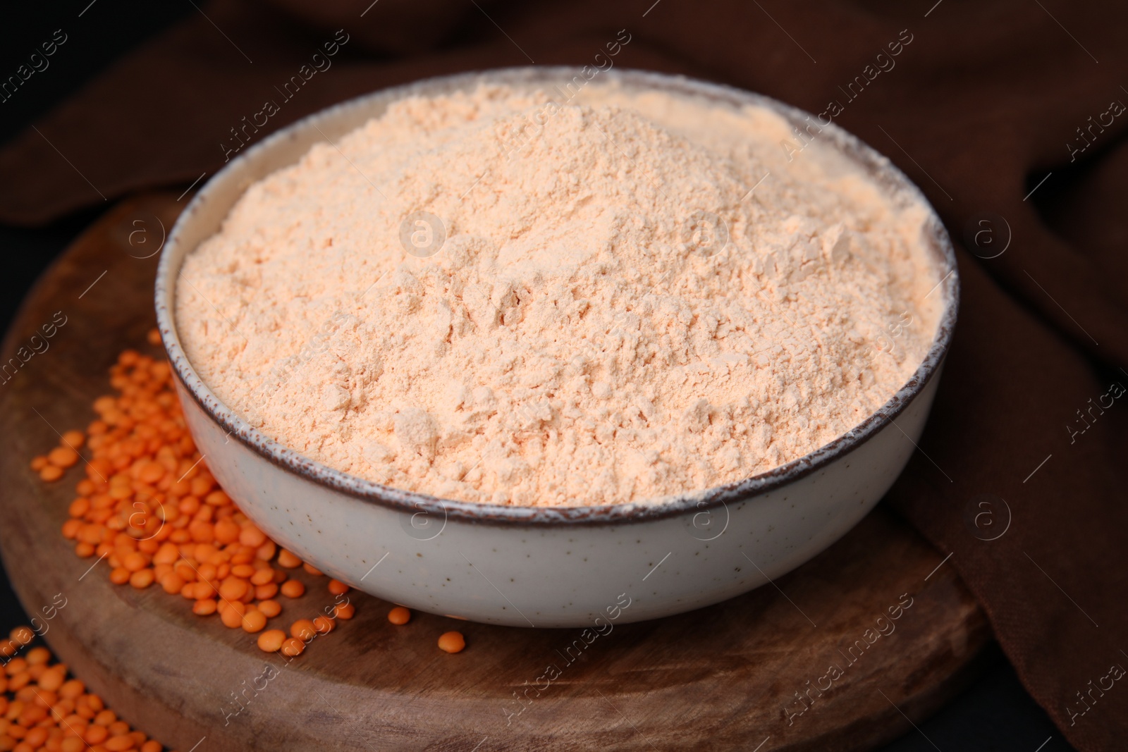 Photo of Bowl of lentil flour and seeds on wooden board, closeup