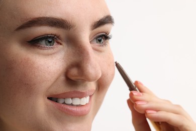 Photo of Smiling woman drawing freckles with pen on white background, closeup