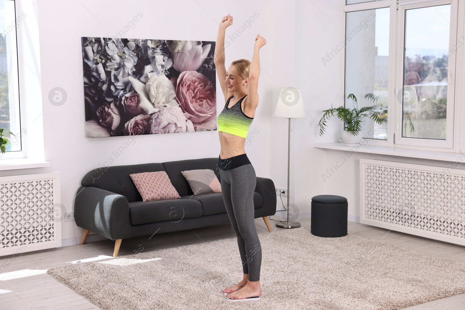 Photo of Happy woman standing on floor scale at home