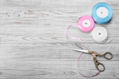 Scissors and colorful ribbons on white wooden table, flat lay. Space for text