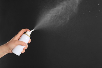 Woman spraying nasal medicine on black background, closeup. Space for text