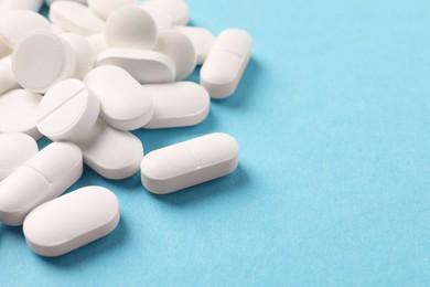 Photo of Pile of white pills on light blue background, closeup. Space for text