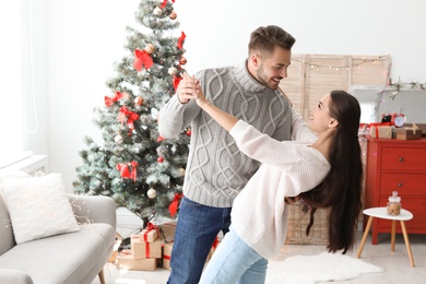 Happy young couple dancing near Christmas tree at home