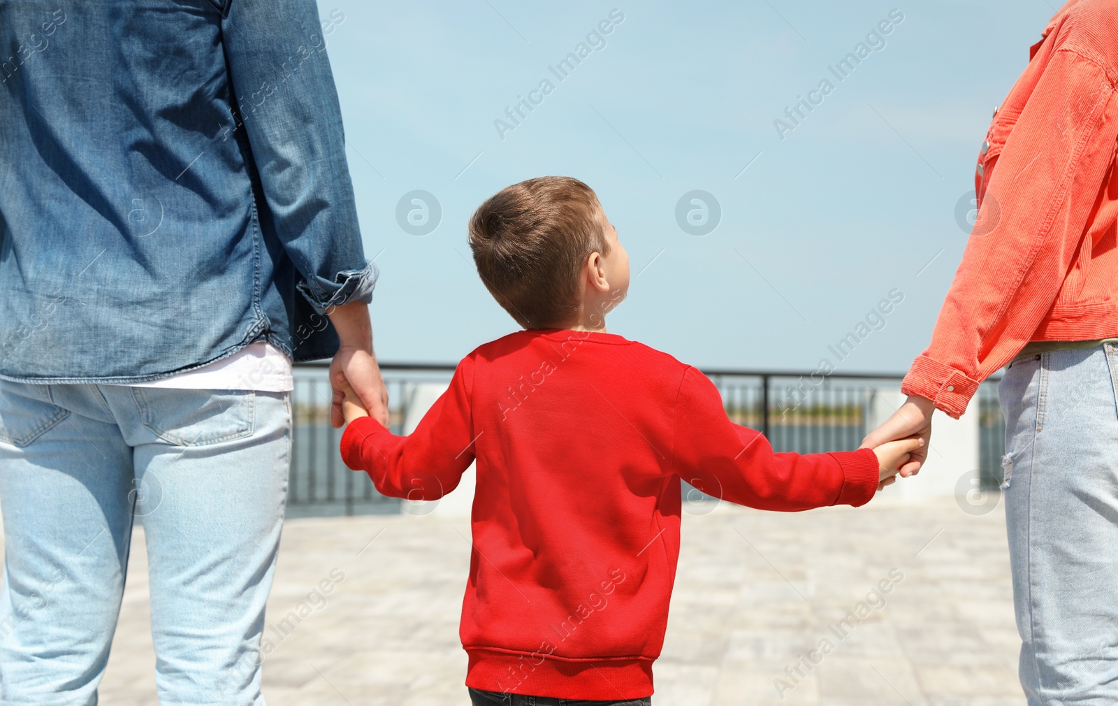 Photo of Little child holding hands with his parents outdoors. Family weekend