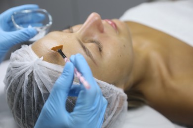 Photo of Cosmetologist applying cosmetic product for chemical peeling on client's face in salon