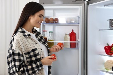 Photo of Young woman taking tomatoes out of refrigerator indoors