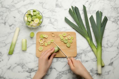 Woman cutting fresh raw leek at white marble table, top view