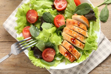 Eating delicious salad with chicken, cherry tomato and spinach at wooden table, top view