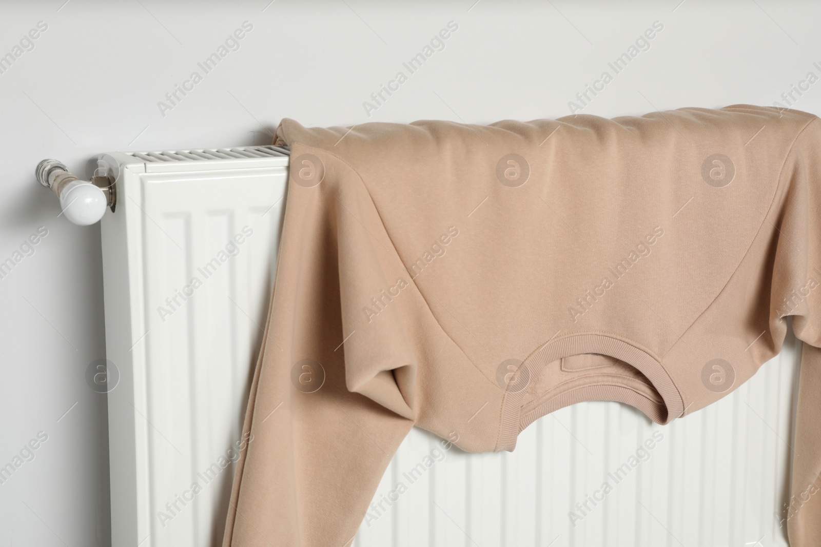 Photo of Clean beige sweatshirt on heating radiator near white wall