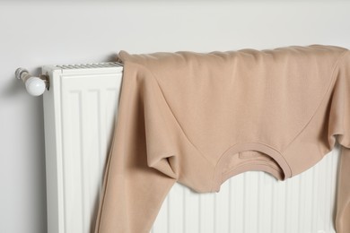 Photo of Clean beige sweatshirt on heating radiator near white wall