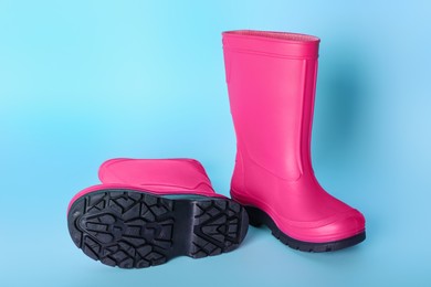 Photo of Pair of bright pink rubber boots on light blue background