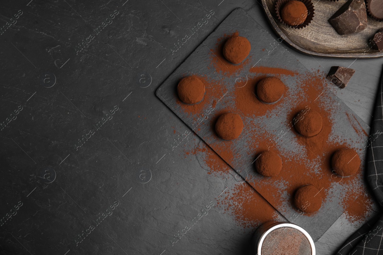 Photo of Delicious chocolate truffles powdered with cocoa on black table, flat lay. Space for text