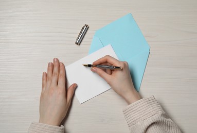 Photo of Woman writing letter at light wooden table, top view