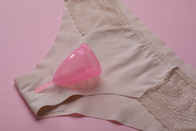Photo of Panties and menstrual cup on pink background, closeup