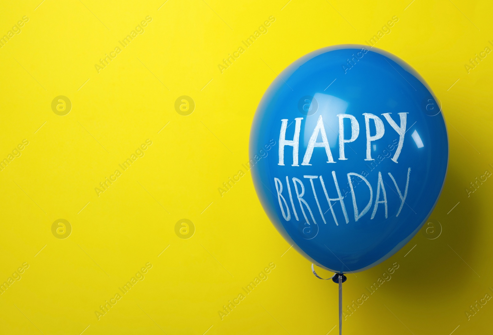 Photo of Blue balloon with words HAPPY BIRTHDAY on yellow background, space for text