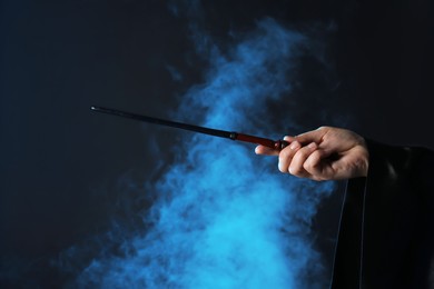 Photo of Magician holding wand in smoke on dark background, closeup