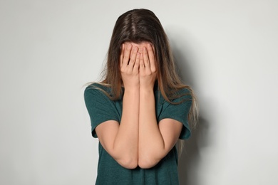 Upset young woman crying against light background