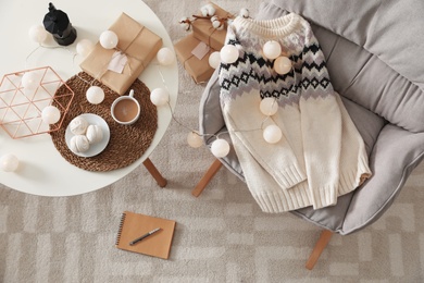 Warm knitted sweater on armchair in cozy living room, flat lay