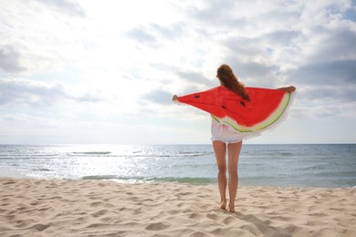 Woman with bright beach towel on sunlit seashore, back view