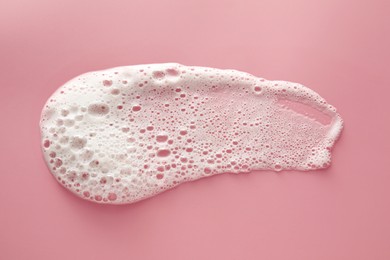 Smudge of white washing foam on pale pink background, top view