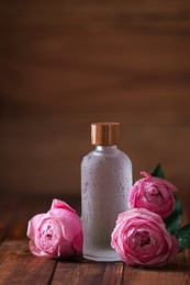 Photo of Bottle of essential rose oil and roses on wooden table. Space for text