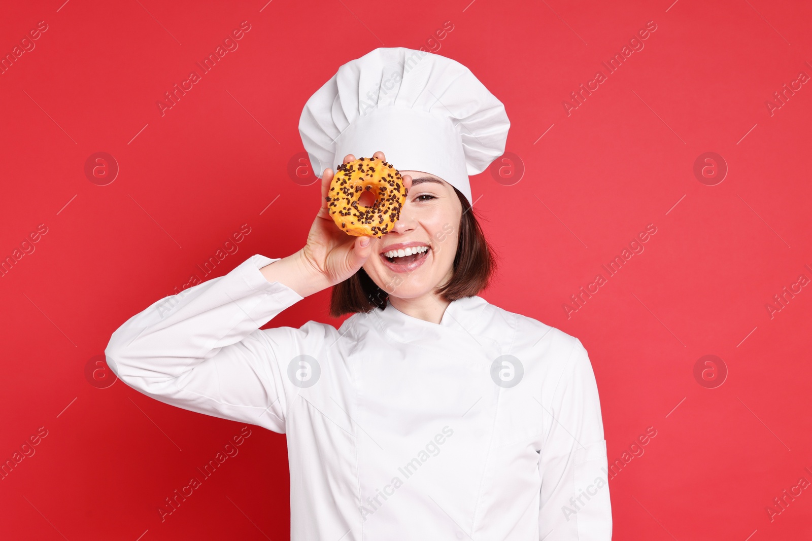 Photo of Happy confectioner with delicious donut on red background