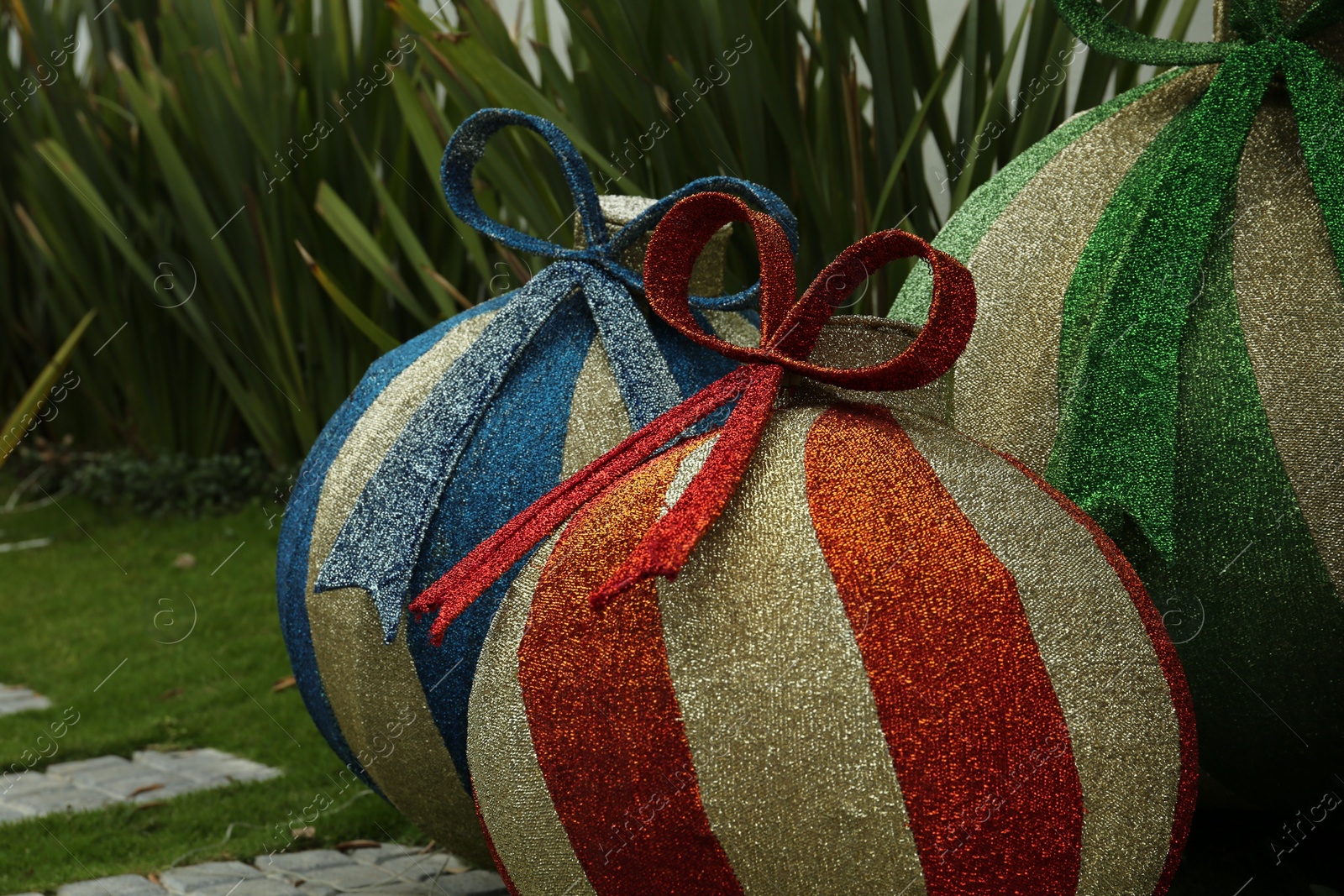 Photo of Beautiful shiny Christmas baubles on green grass outdoors, closeup. Festive street decorations