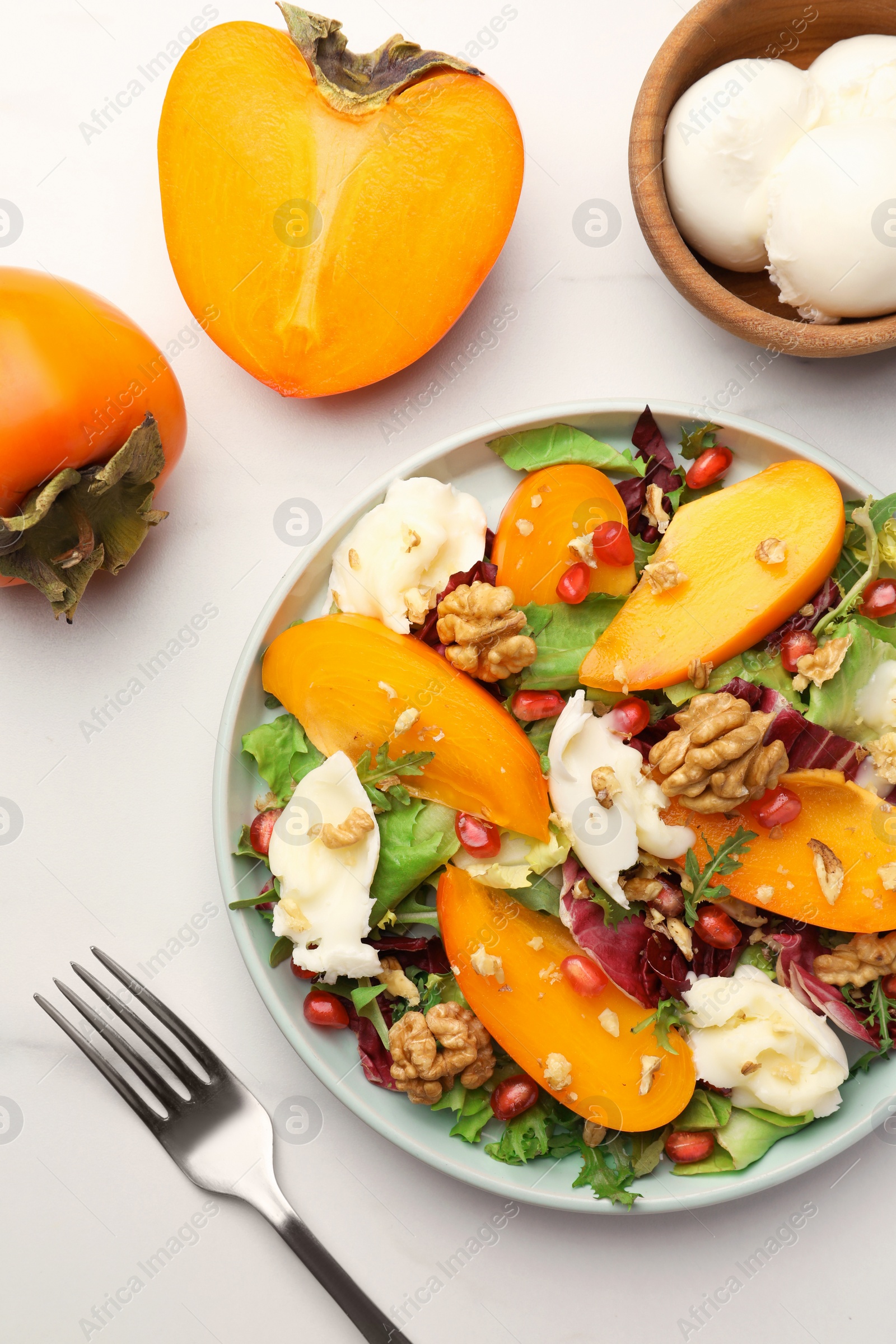 Photo of Delicious persimmon salad with cheese and pomegranate served on white table, flat lay