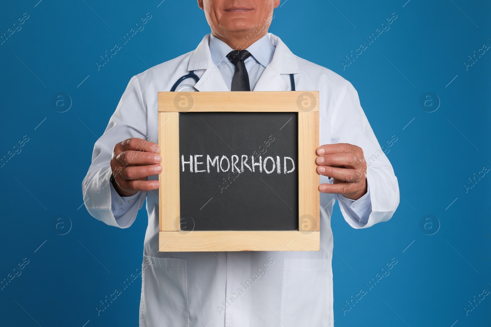 Photo of Doctor holding blackboard with word HEMORRHOID on blue background, closeup