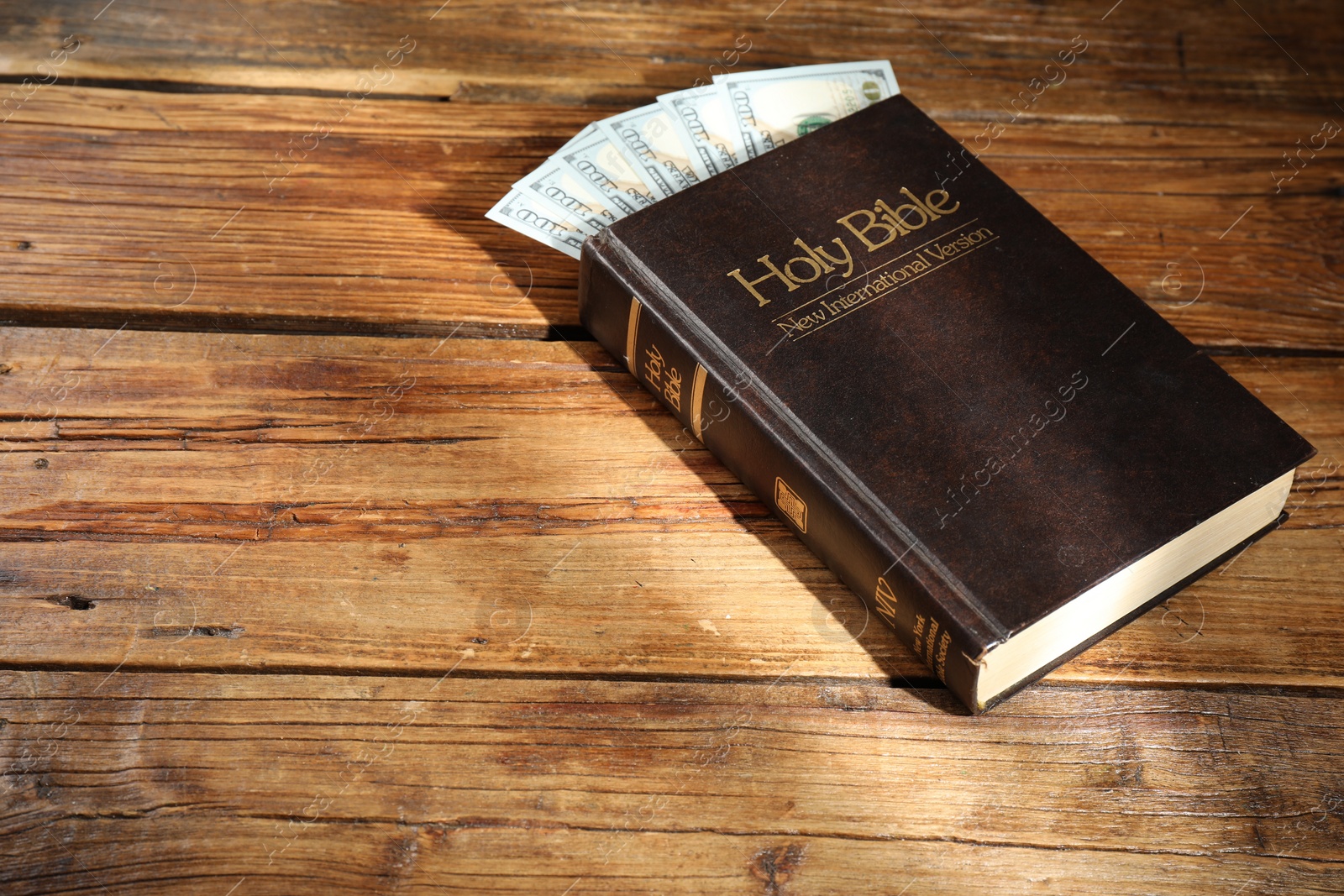 Photo of Holy Bible and money on wooden table. Space for text