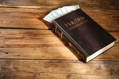 Photo of Holy Bible and money on wooden table. Space for text