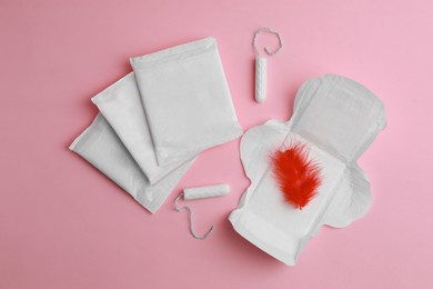 Photo of Menstrual pads, tampons and feather on pink background, flat lay
