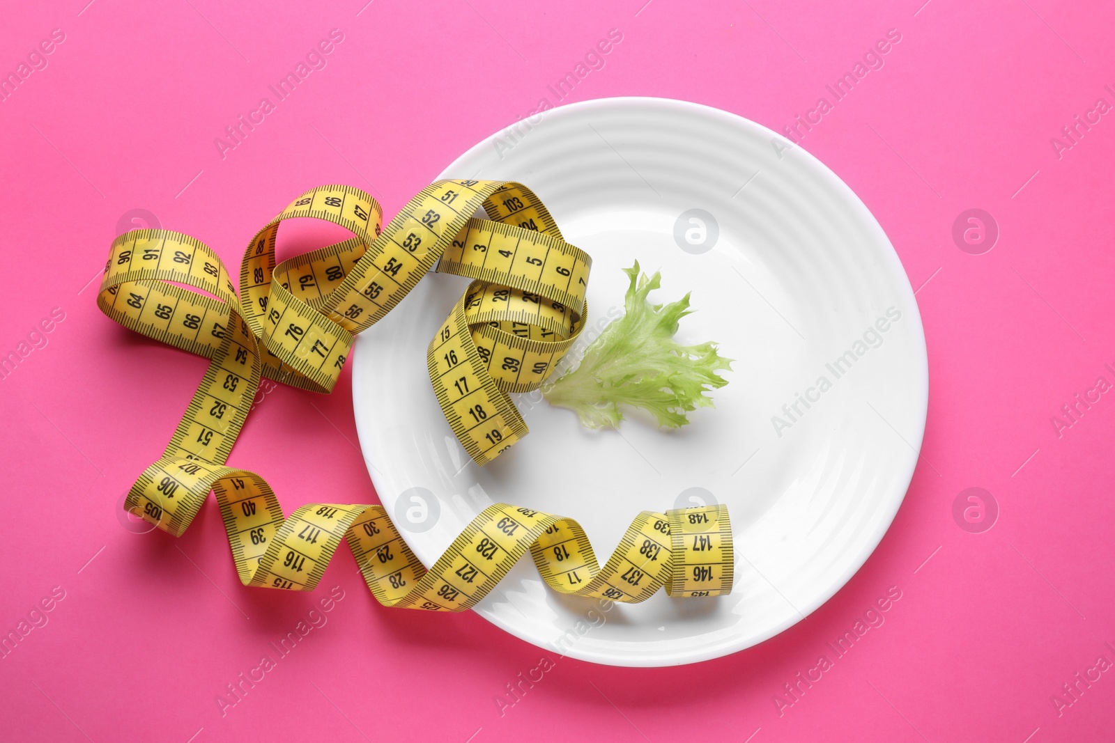 Photo of Plate with measuring tape and lettuce leaf on pink background, top view. Diet concept