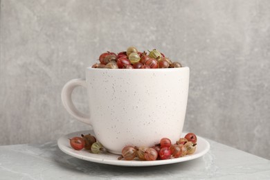 Photo of Cup with ripe gooseberries on light grey marble table