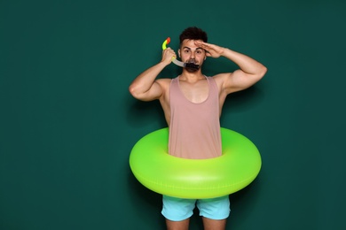 Photo of Funny young man with bright inflatable ring on dark green background