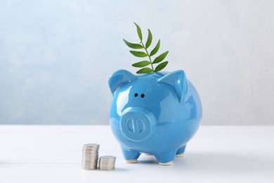 Financial savings. Piggy bank with green twig and stacked coins on white table