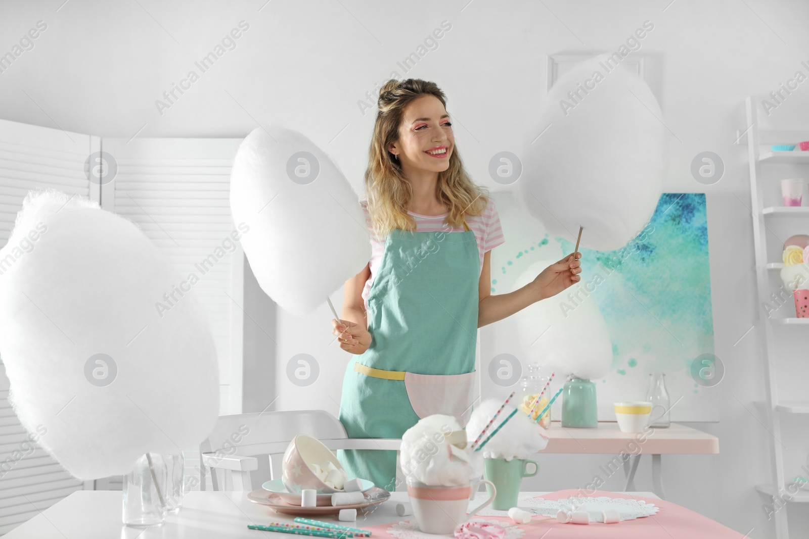 Photo of Happy young woman with cotton candy and sweets on table in room