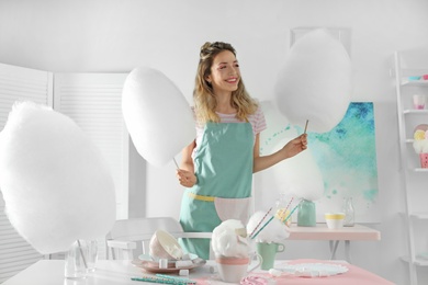 Happy young woman with cotton candy and sweets on table in room