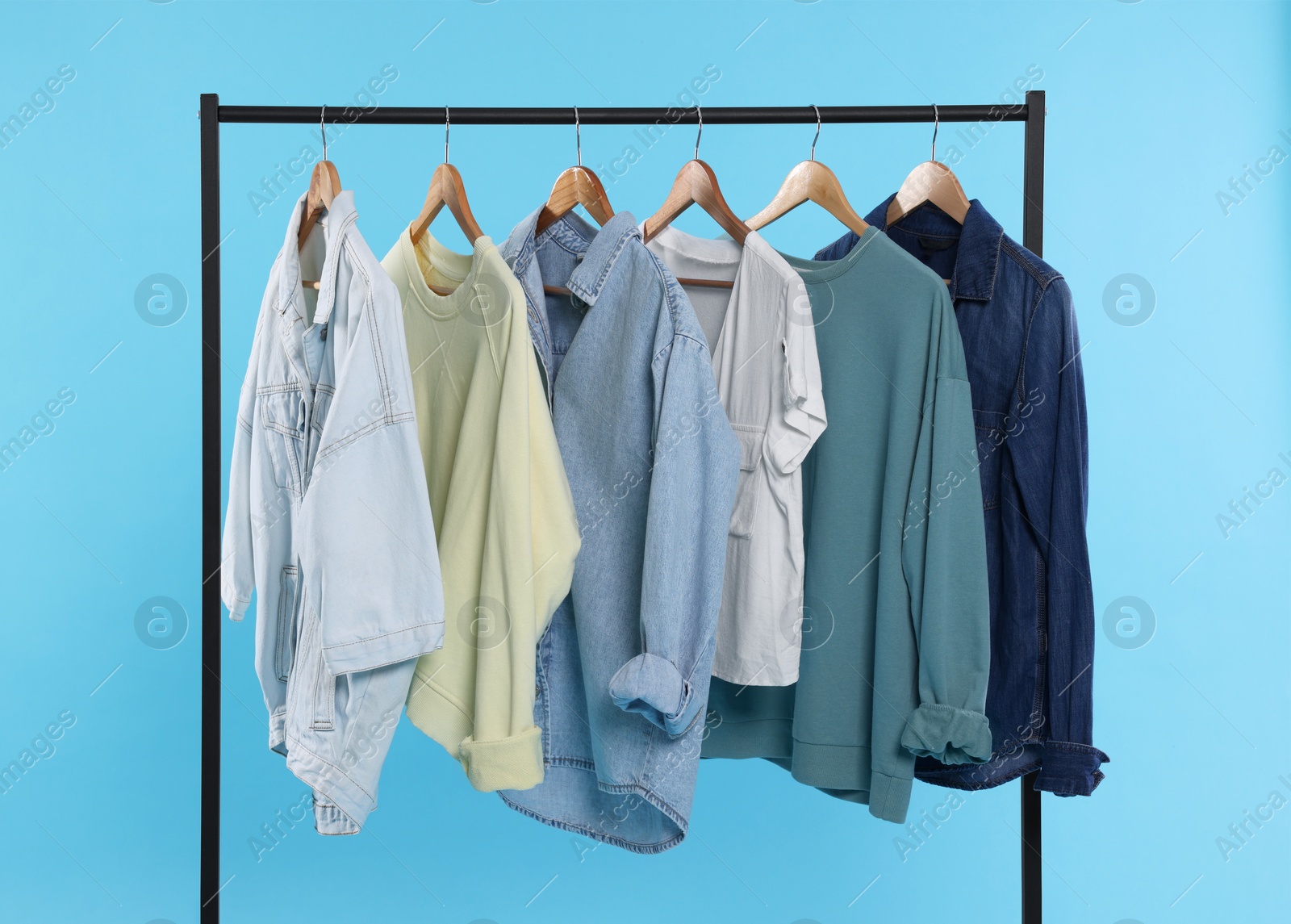 Photo of Rack with stylish clothes on wooden hangers against light blue background