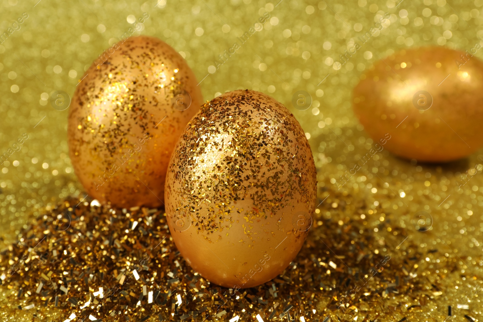 Photo of Shiny golden eggs with glitter on yellow background, closeup