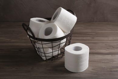 Photo of Soft toilet paper rolls in metal basket on wooden table