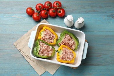 Raw stuffed peppers in dish and tomatoes on wooden table, flat lay