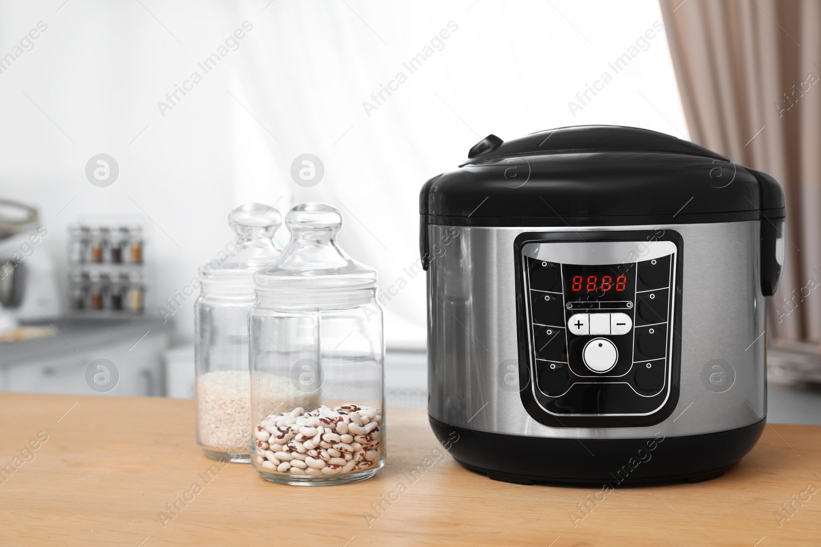 Photo of Jars with rice and beans near modern multi cooker on table in kitchen