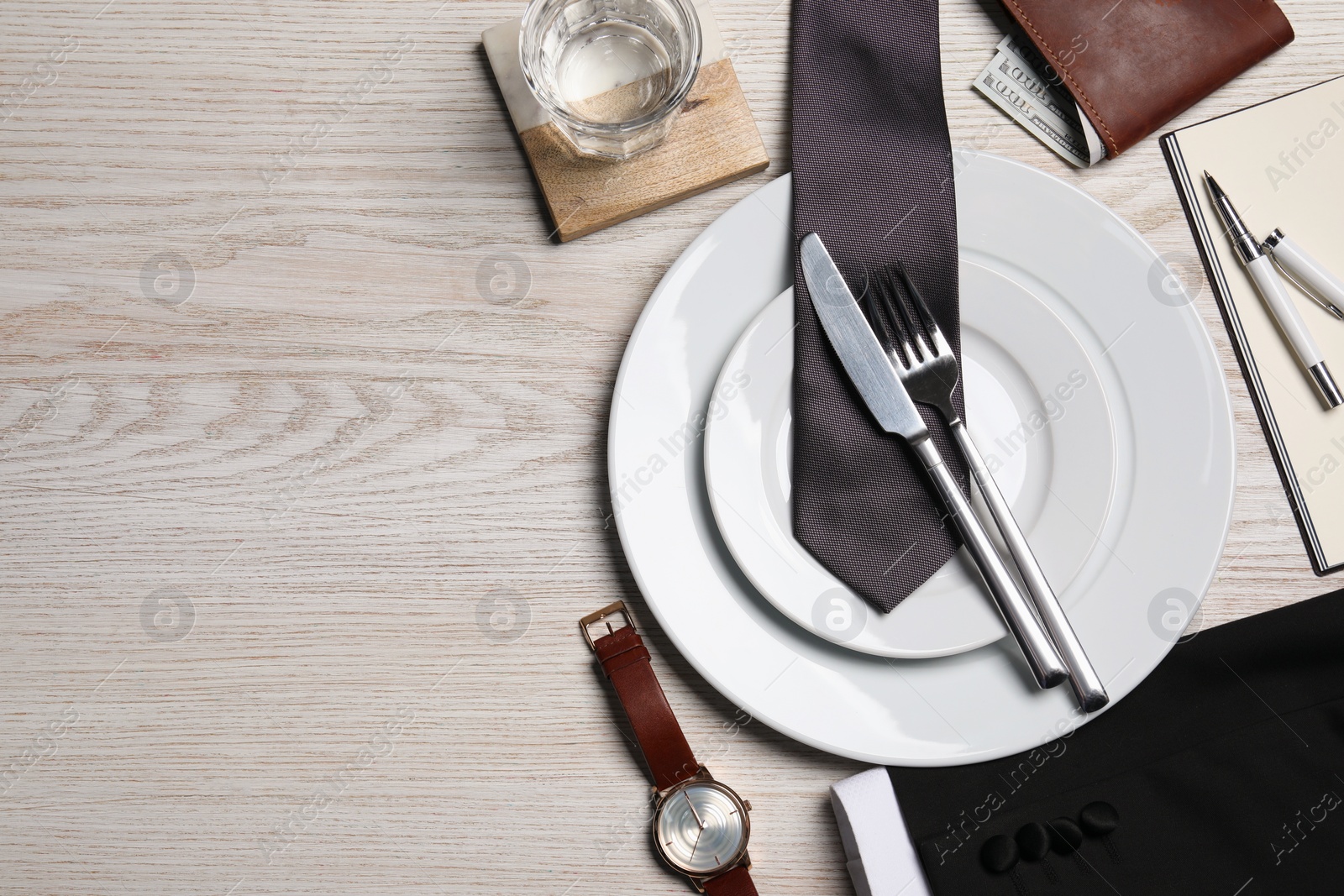 Photo of Business lunch concept. Plates, cutlery, glass of water, tie and watch on wooden table, flat lay with space for text