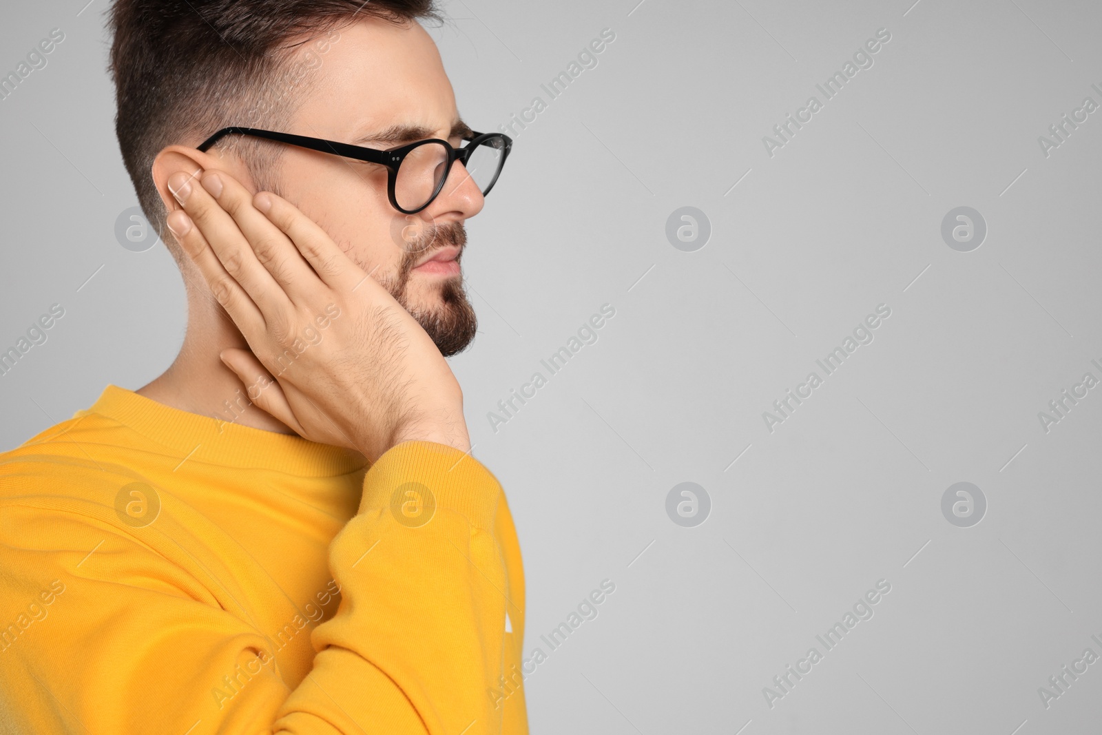 Photo of Young man suffering from ear pain on light grey background. Space for text