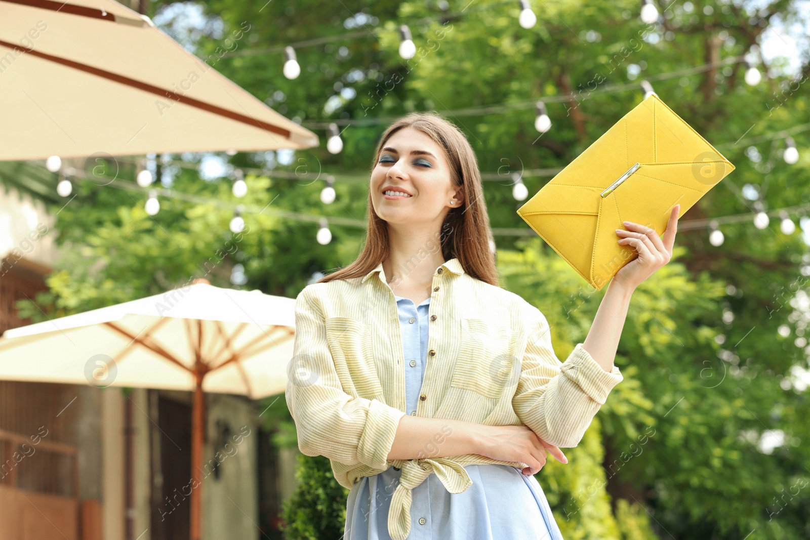 Photo of Beautiful young woman with elegant envelope bag outdoors on summer day