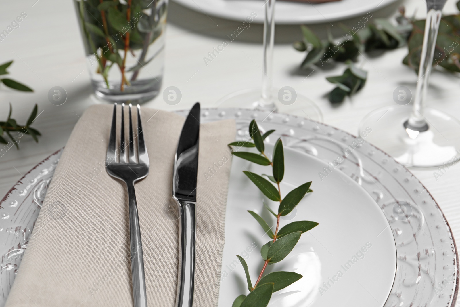 Photo of Stylish setting with cutlery and eucalyptus leaves on white wooden table, closeup