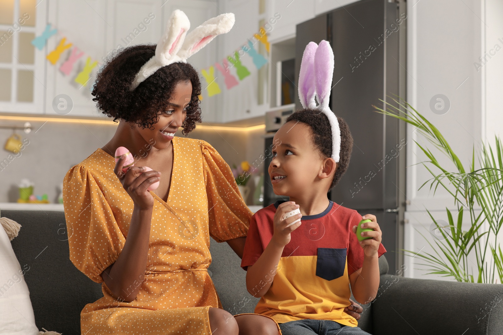 Photo of Happy African American mother and her cute son with Easter eggs in kitchen