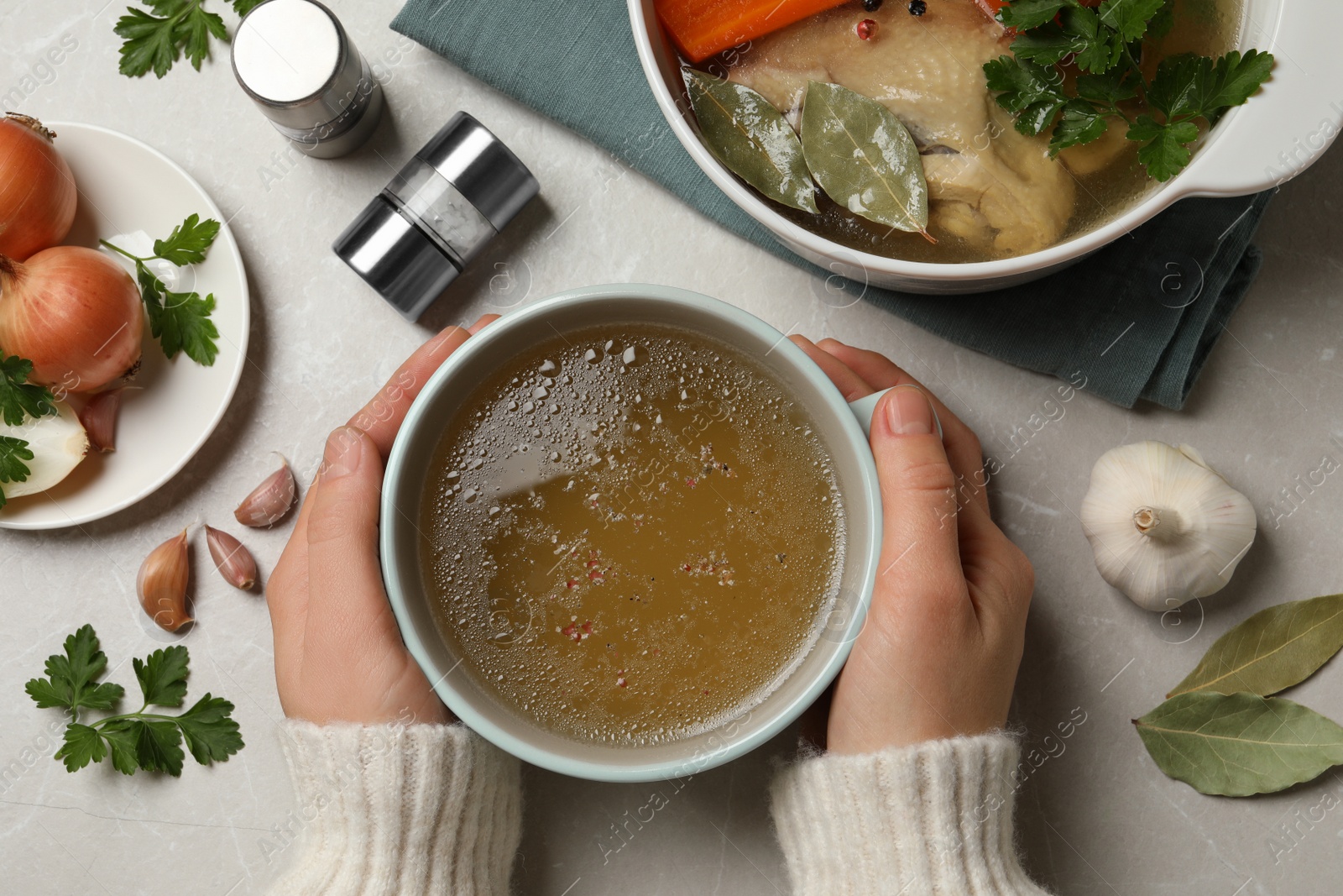 Photo of Woman with cup of hot delicious bouillon at light grey table, top view